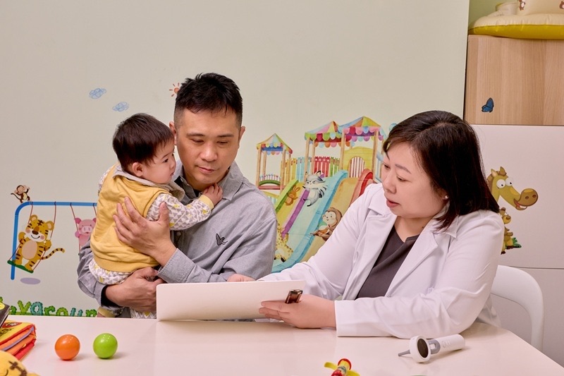 以法大聽力師在兒童友善的評估室中，為爸爸懷裡還不會說話的嬰兒進行助聽器選配諮詢