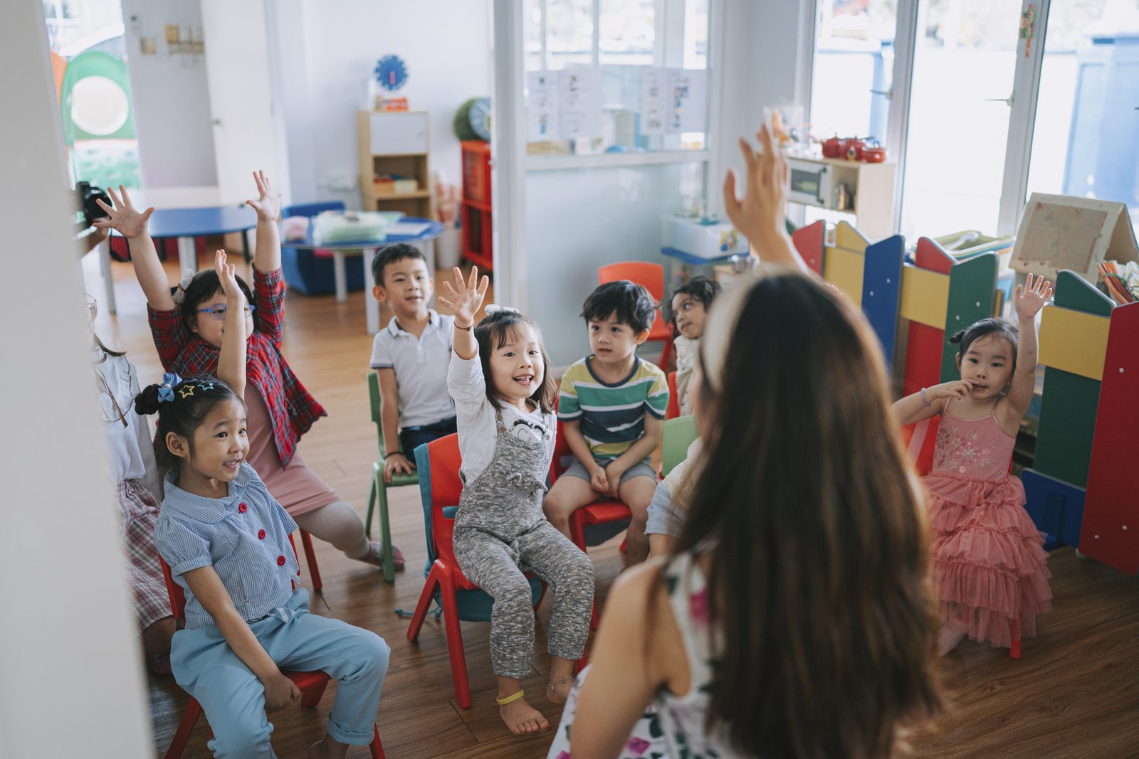 幼兒園教室裡，小朋友們舉手回答老師問題