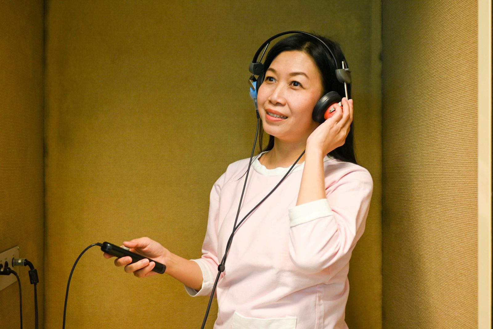 女性在隔音室戴耳機、手握按鈕做聽力檢查