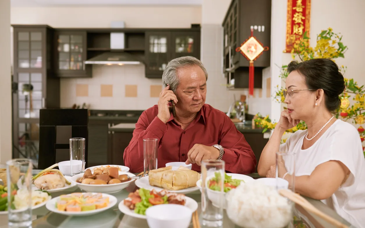 餐桌前，一位長輩正在講電話，家人在一旁看著